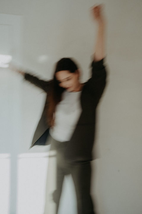 Frau tanzt mit erhobenen Armen im hellen Raum.