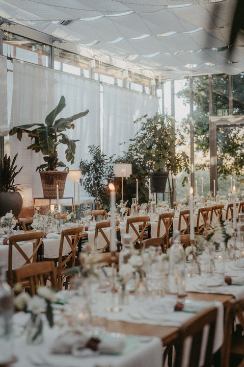 Detailshot einer stilvollen Hochzeitstafel im Glashaus mit Kerzen, Grünpflanzen und warmem Licht – moderne, natürliche Atmosphäre.