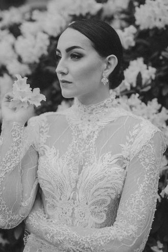 Porträt der Braut vor üppigen weißen Blüten, elegant und ruhig in ihrem Spitzenkleid.