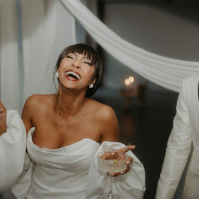 Braut und Bräutigam lachen während Apere mit Glas in der Hand