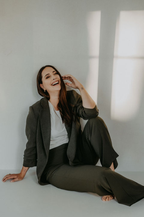 Frau sitzt lachend am Boden in modernem Studio mit natürlichem Licht.