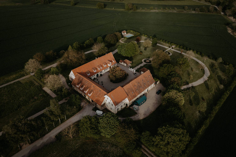 Drohnenaufnahme eines weitläufigen historischen Gutshofes, umgeben von grünen Feldern.
