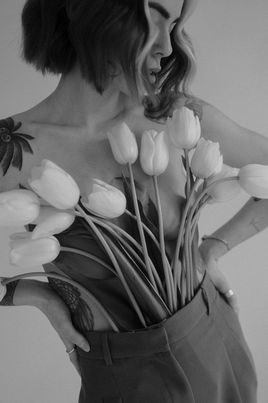 Künstlerische Nahaufnahme einer Frau mit weißen Tulpen vor dem Oberkörper.