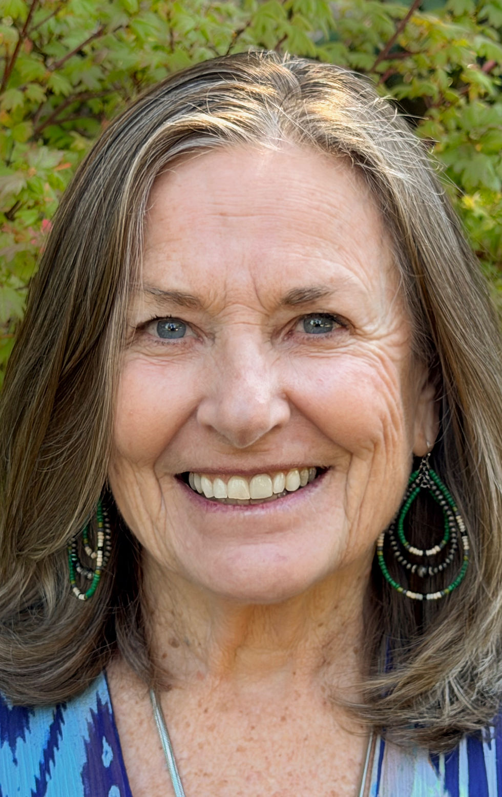 Portrait of Debra smiling in front of green foliage, landscape orientation, warm natural colors.