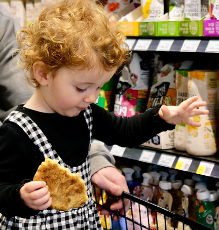 Toddler riding in grocery cart and grabbing baby food off the shelf