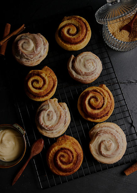 vertical-shot-of-delicious-cinnamon-rolls-with-small-bowl-of-white-glaze-on-black-table_ed