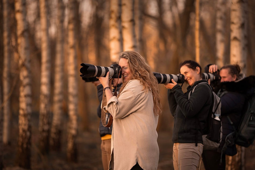 Eliane van Schaik laughing behind her camera among photographers with long lenses in a birch forest