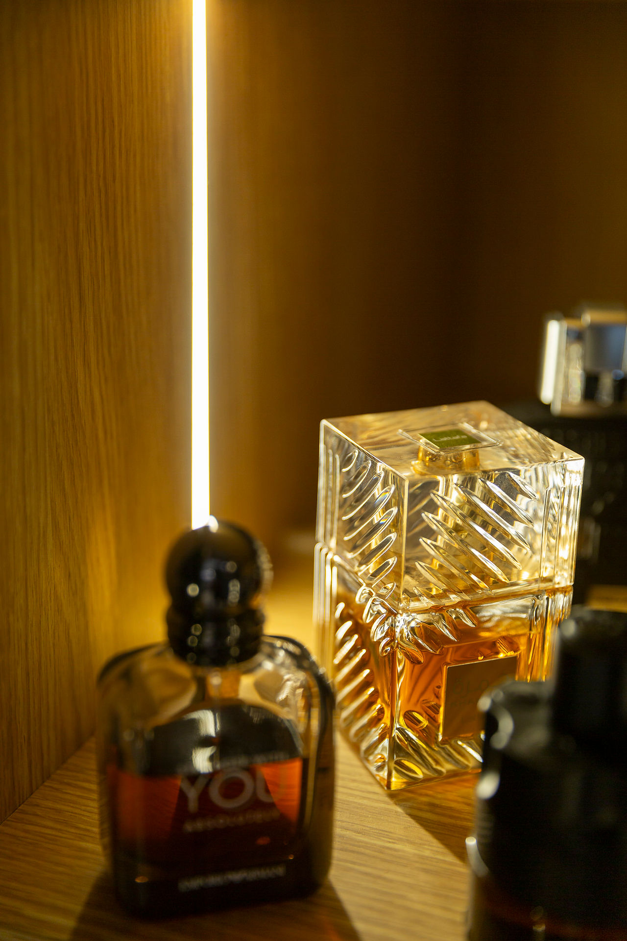 Two perfume bottles, one labeled YOU ARMANI, on illuminated shelf.