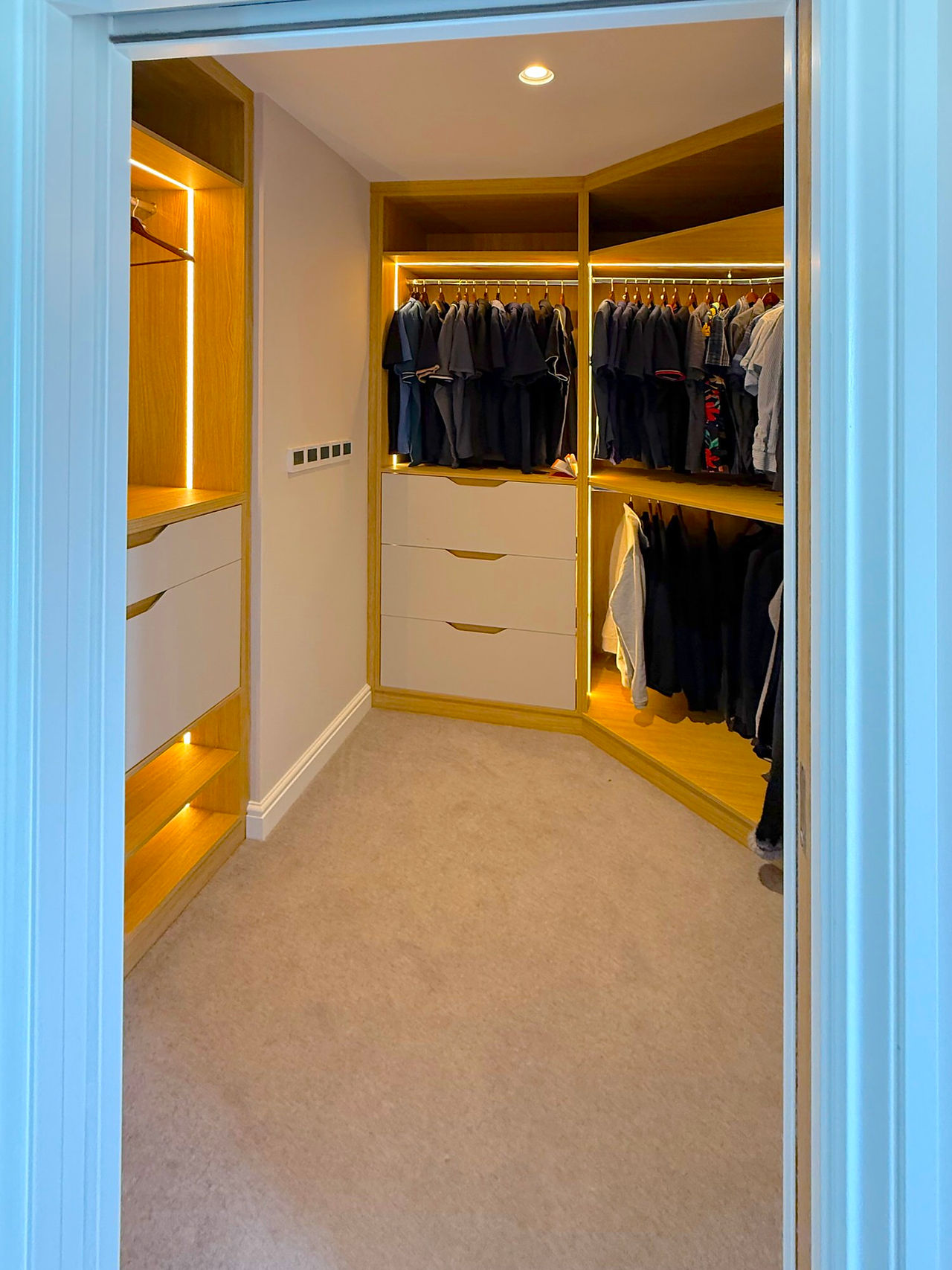 Custom walk-in closet with integrated lighting, shelves, drawers, and hanging clothes.