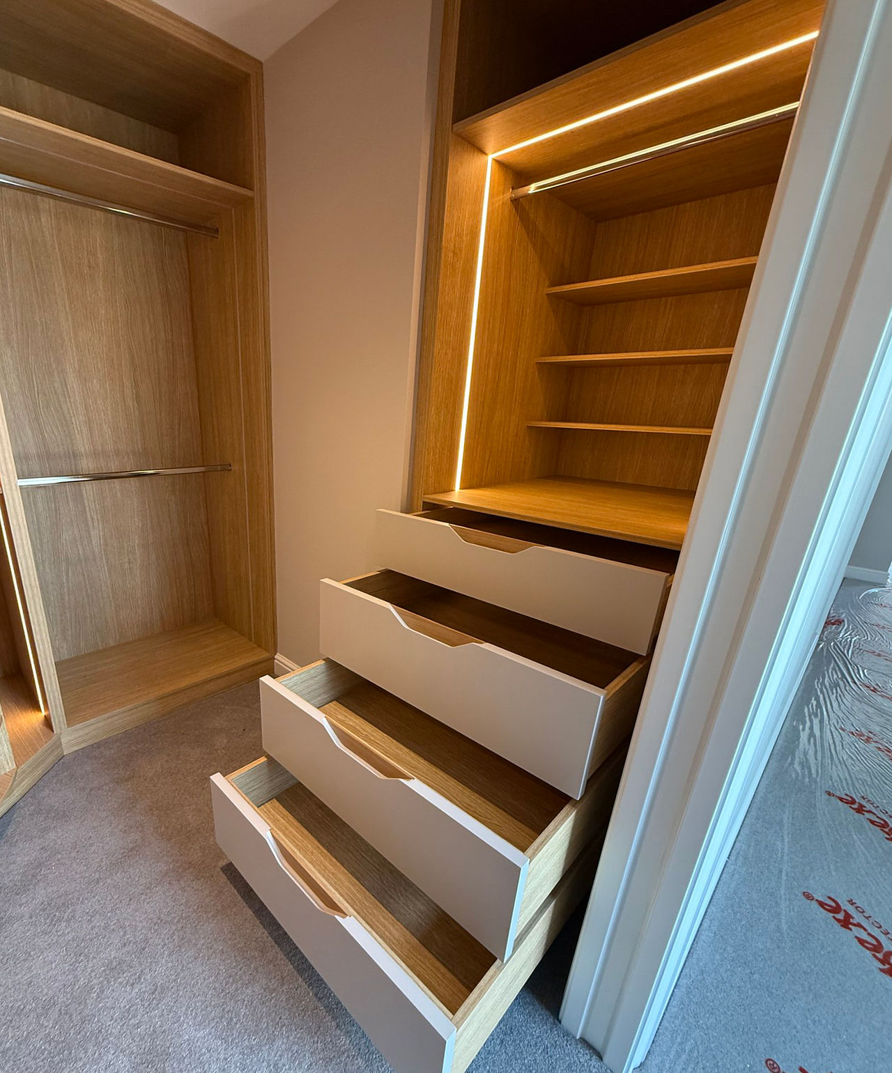 Modern bespoke walk-in closet with lit shelving and open drawers.