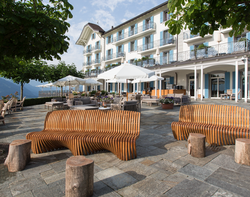 Outdoor hotel seating area with wooden benches and umbrellas near a building.