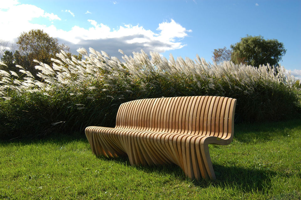 Wooden bench on green grass with tall plants and blue sky background Diamond Tropical Hardwoods
