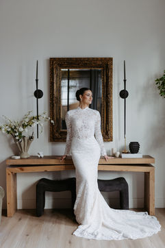 Bride with an all-lace fit and flare dress, framed in by an antique gold mirror behind her, looking out the window. Portrait at Hidden Grove Estate in Williamston, Michigan. Best Williamston Photographers. True to color, timeless photography. Grand Rapids Documentary Wedding Photographer.