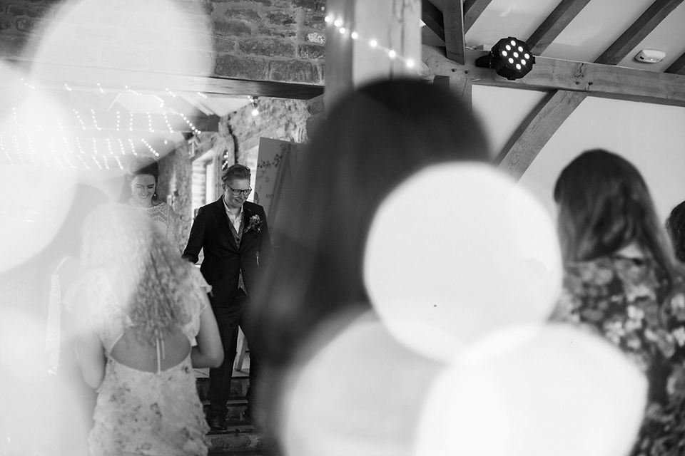 Natural, relaxed wedding photography at Dodford Manor, Northamptonshire. Bride and bride are greeted into the wedding breakfast room walking down some stairs. Black and white creative photograph with bokeh lights in the foreground. Relaxed wedding photography. Leicester wedding photography. Covering wedding photography in Rutland, Northamptonshire, Lincolnshire, Nottinghamshire.