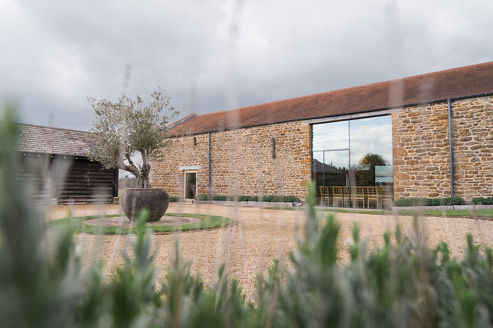 Wedding photography at Dodford Manor, Northamptonshire. The front of Dodford Manor with olive tree centre piece, gravel drive and full height window on the rustic barn wedding venue. Local wedding photography. Leicestershire wedding photographer. Covering wedding photography in Rutland, Warwickshire, Staffordshire, Northamptonshire, Lincolnshire, Nottinghamshire.