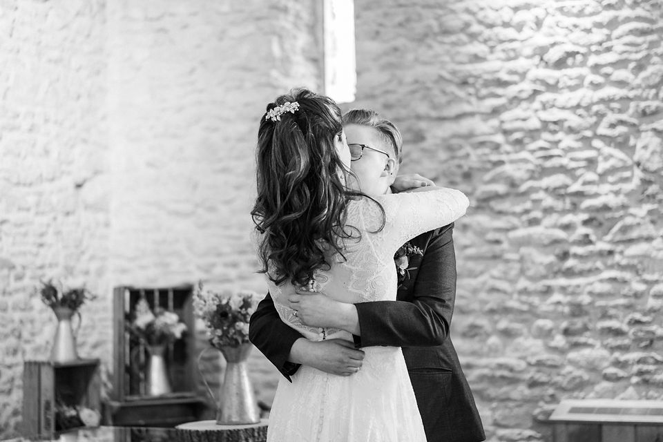 Black and white first kiss photo by natural wedding photographers Darley and Underwood. Gay wedding with kiss and hug around lace wedding dress. Happy wedding photography.