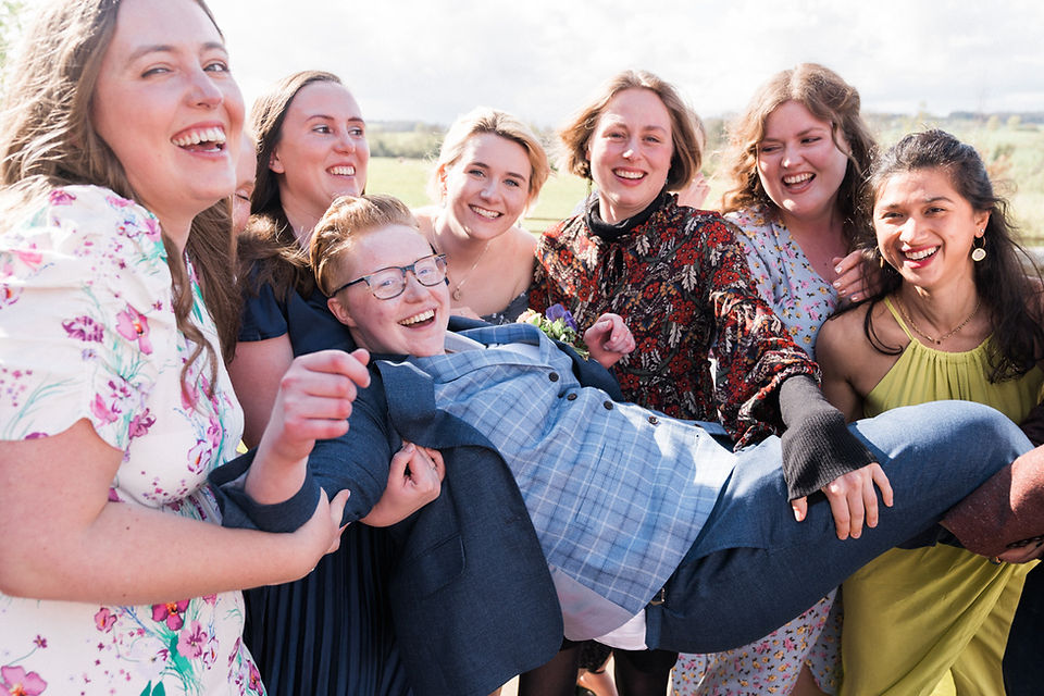 Fun wedding photography at Dodford Manor, Northamptonshire, with bride in blue tailored suit being lifted up by friends in the courtyard. Leicester wedding photographer. Covering wedding photography in Rutland, Derbyshire, Northamptonshire, Darley and Underwood Photography.