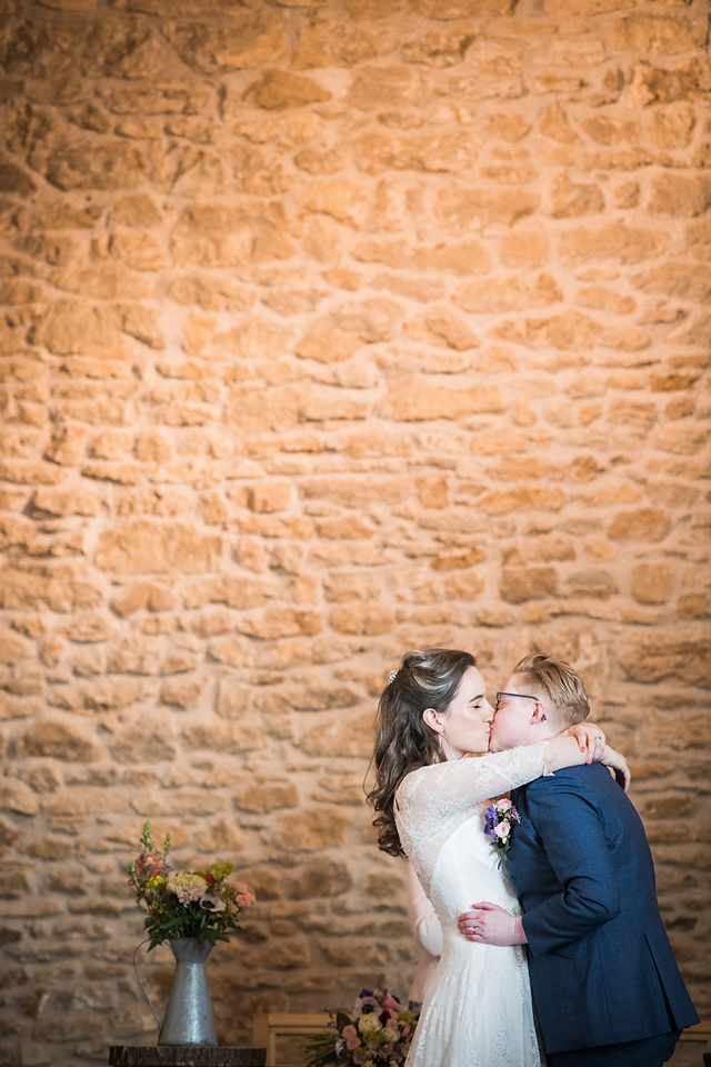 Amazing first kiss photograph at Dodford Manor wedding ceremony. Gay wedding with two doctors at Dodford Manor. Key worker wedding competition. Stone wall backdrop. 