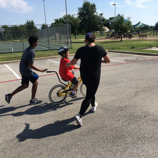 Two Volunteers Run Alongside a New Bike Rider