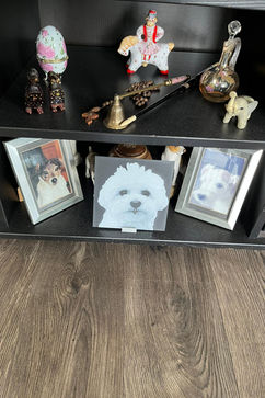 3D-geprint portret van een witte hond op een zwarte plank, tussen twee hondenfoto’s en decoratieve objecten.