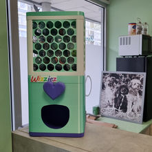 Groen en paarse 3D-geprinte ballenmachine met het Wizziez-logo op een balie in een trimsalon.