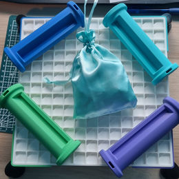 Vier gekleurde 3D-geprinte buisonderdelen van een waterleidingspel rond een satijnen zakje op een rasterondergrond.
