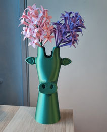 Roze en paarse 3D-geprinte bloemen in een groene 3D-geprinte vaas op een lichte ondergrond.