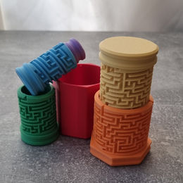 3D-geprinte doolhofpuzzel met meerdere stapelbare levels in regenboogkleuren, met een rood bakje op de achtergrond.