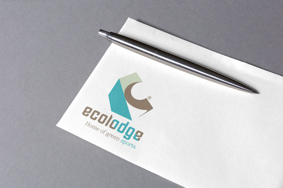 Foto des ecolodge Sports Logos auf einer Business Card, oben an der Karte klemmt ein silberner Kugelschreiber.