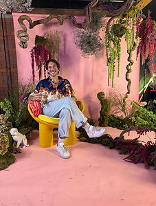 Florist seated on a yellow chair inside a pink floral installation with hanging foliage
