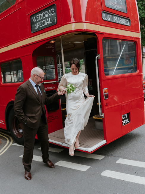 Bride and groom getting off a vintage red double decker bus on their wedding day