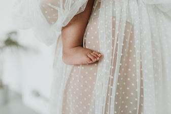 Maternity shoot of a mother and her baby, there is a bare baby's foot against her leg.