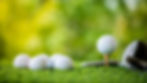 Close-up of golf balls on green turf with one ball on a wooden tee and blurred greenery in the background.
