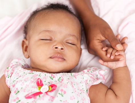 A baby is sleeping in a pink dress with her hand on it.