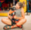 A woman in a striped tank top sits cross-legged, lovingly hugging a black dog wearing an orange bandana.
