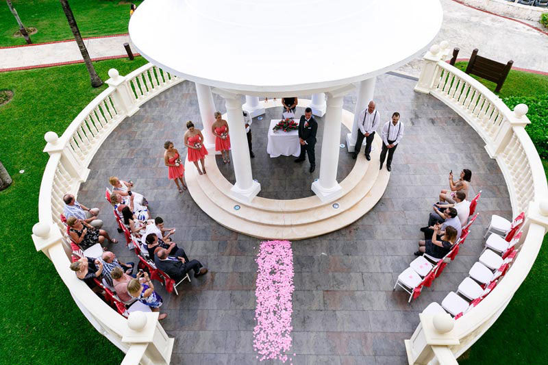 Drone view of a circular wedding ceremony set up in an outdoor white gazebo.