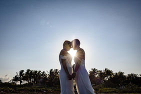 Sunset silhouette of the brides kissing with light shining between them.