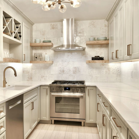 Glam kitchen renovation with grey cabinets, open shelving, rustic white tile, quartz countertops with veining, and bronze hardware.