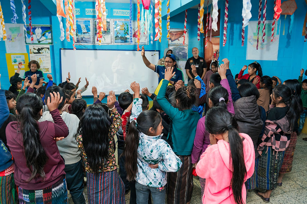 Children raising their hands in a classroom as the Jesus Film plays behind them—a moment of engagement and Gospel clarity during Reel Joy outreach