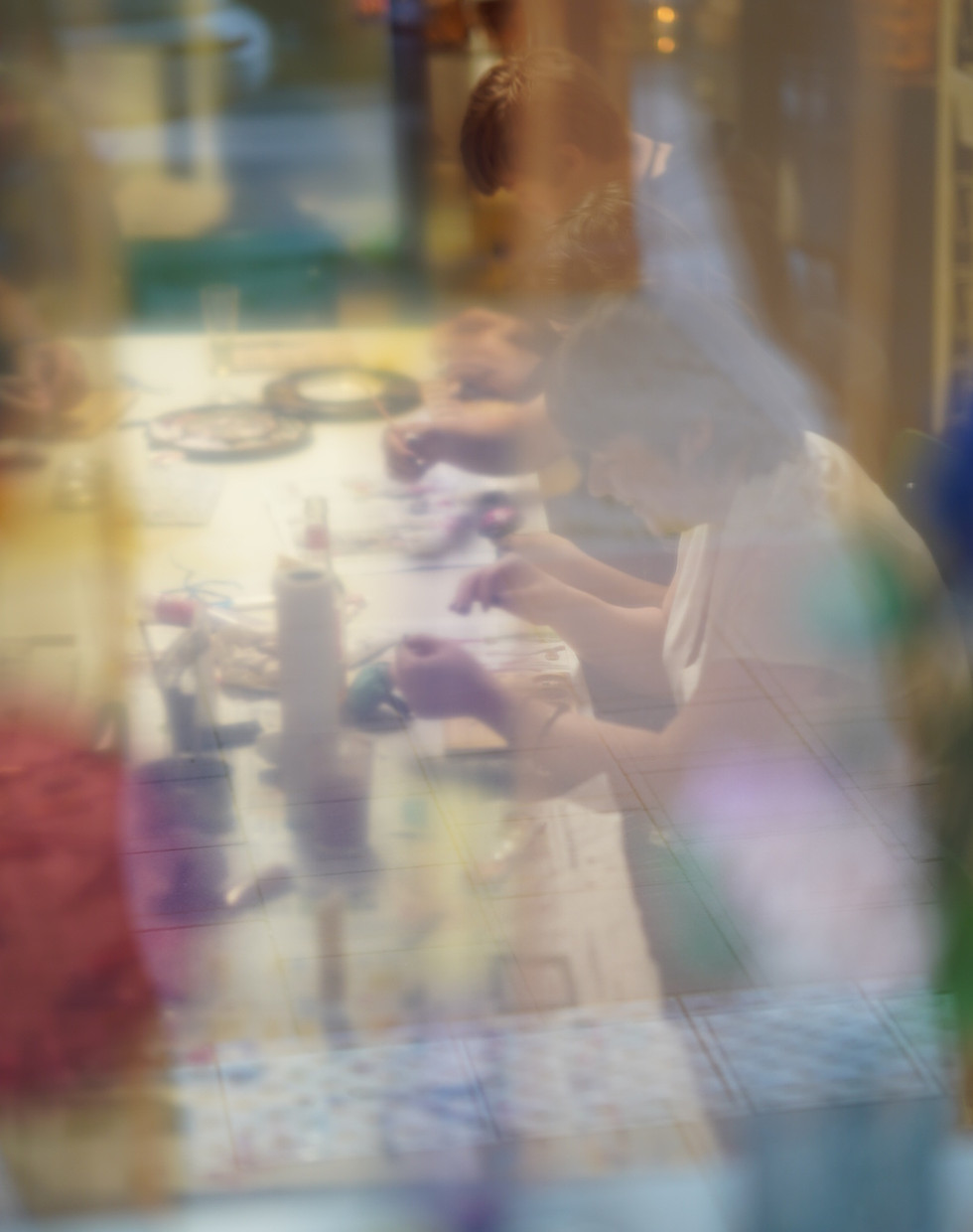 Blick durch ein Fenster mit transparentem Vorhang auf Menschen am Workshoptisch, die basteln.