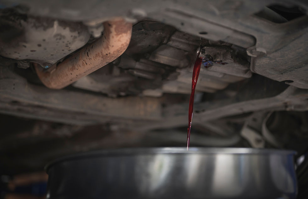 Red fluid drains from a car's underside into a metal container in a dimly lit garage, showing oil change or maintenance process.