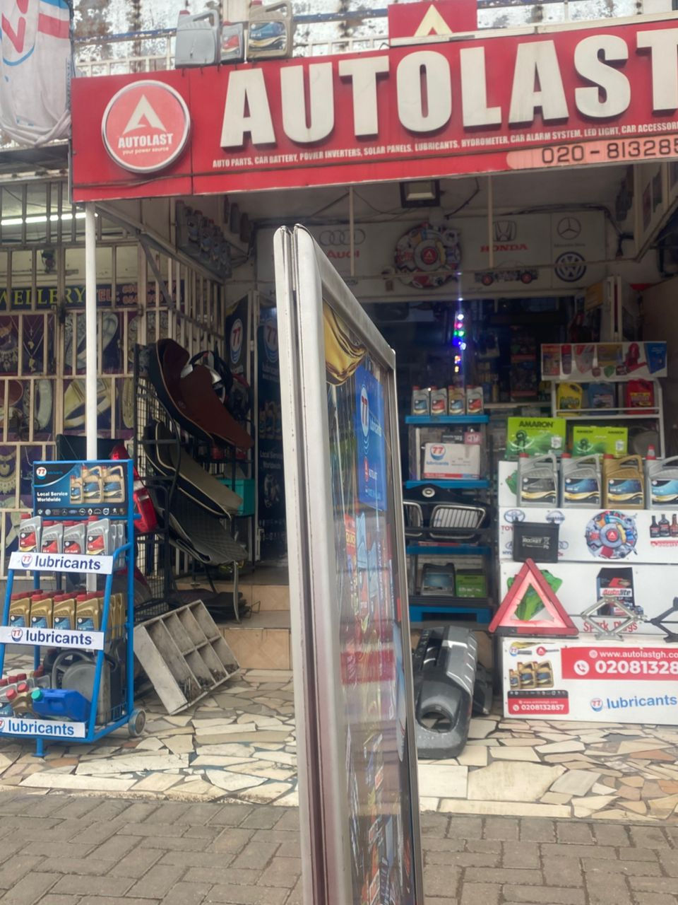 Exterior of AUTOLAST store with red signage. Displays various auto products like lubricants and solar panels. Bright, commercial setting.