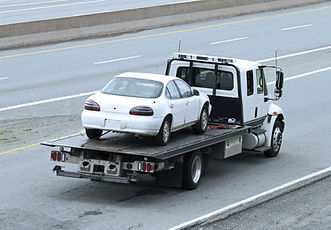 White car on a flatbed tow truck on a highway.