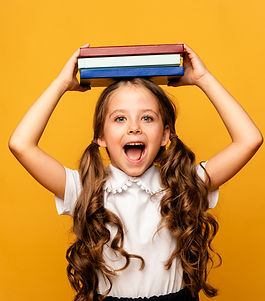 Funny happy Preschool Child girl with Book on Head and Bag on Yellow Background, Copy Spac
