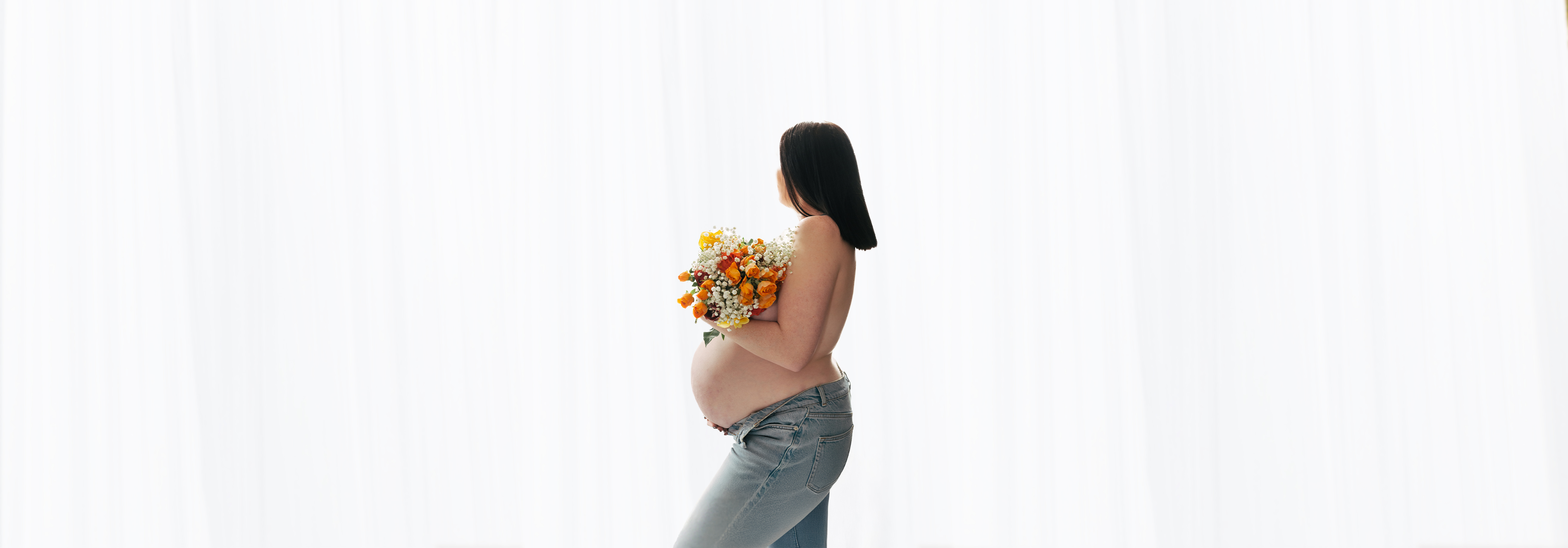 Séance photo grossesse à domicile dans l'oise, jeune maman de profil avec ventre rond et bouquet de fleurs, seance réalisé par boréale photo 