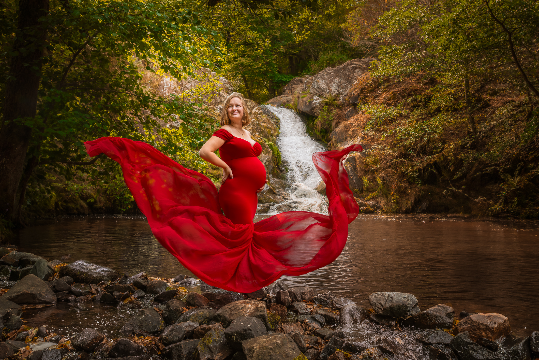 Séance photo grossesse en extérieur dans l’Oise, future maman portant une robe au voilage flottant devant une cascade