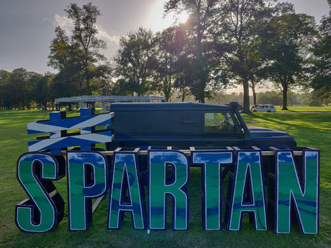 Matte black Land Rover DJ Truck providing event sound at Spartan OCR in Scotland, featuring large-scale branded course obstacles and outdoor festival production.