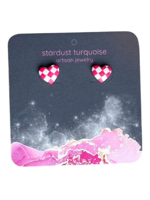 A pair of pink and white checkered heart stud earrings on a dark decorative earring card.