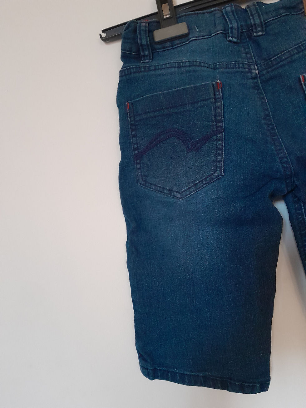 Miniature : Gros plan sur un jean bleu avec une poche arrière, contre un mur blanc