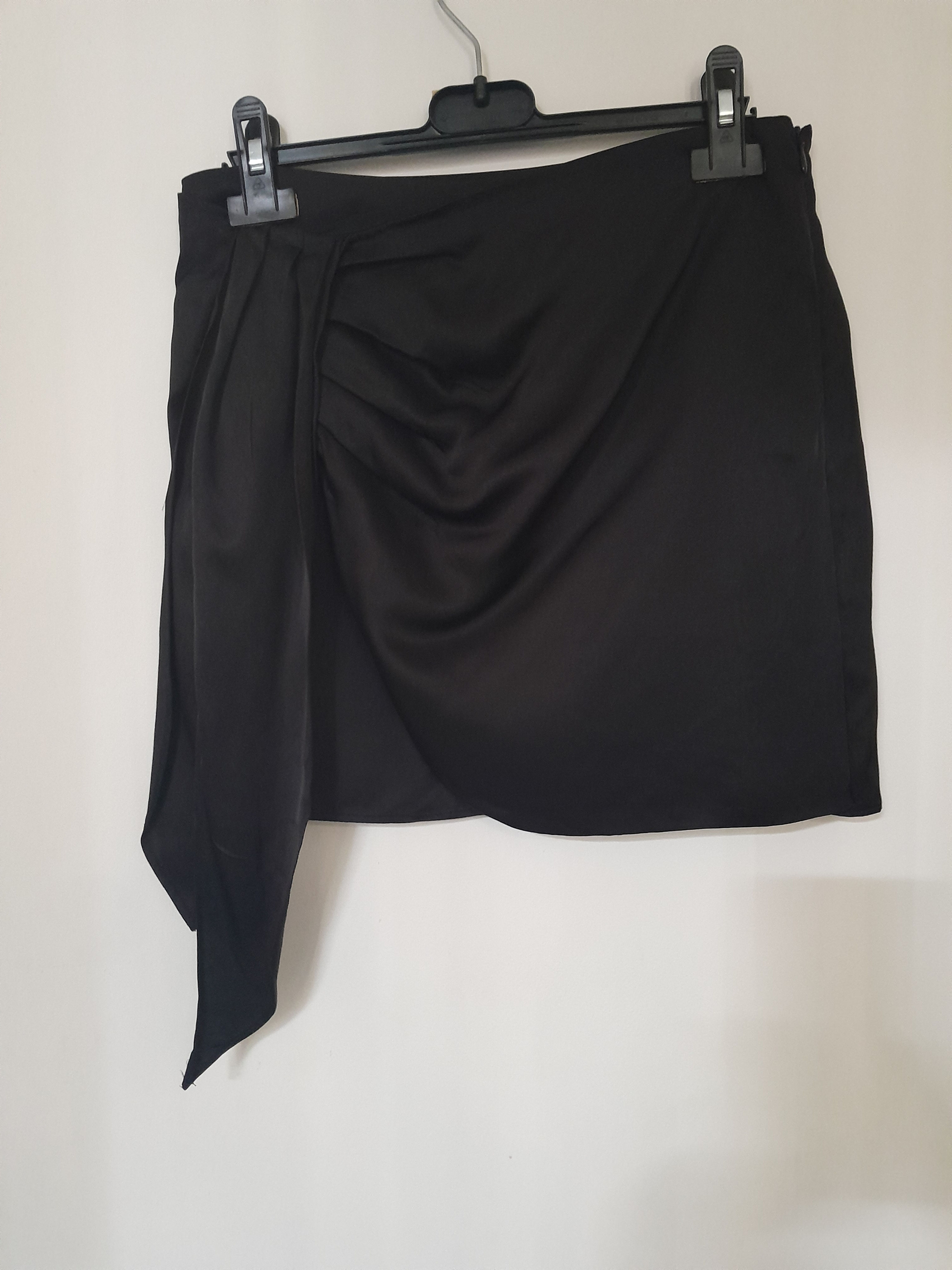 Jupe noire drapée sur cintre, détail de nœud. Vêtement de mode prêt à porter.